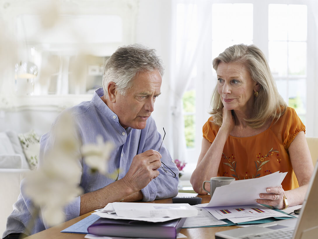 Two elderly people looking at bills around a table
